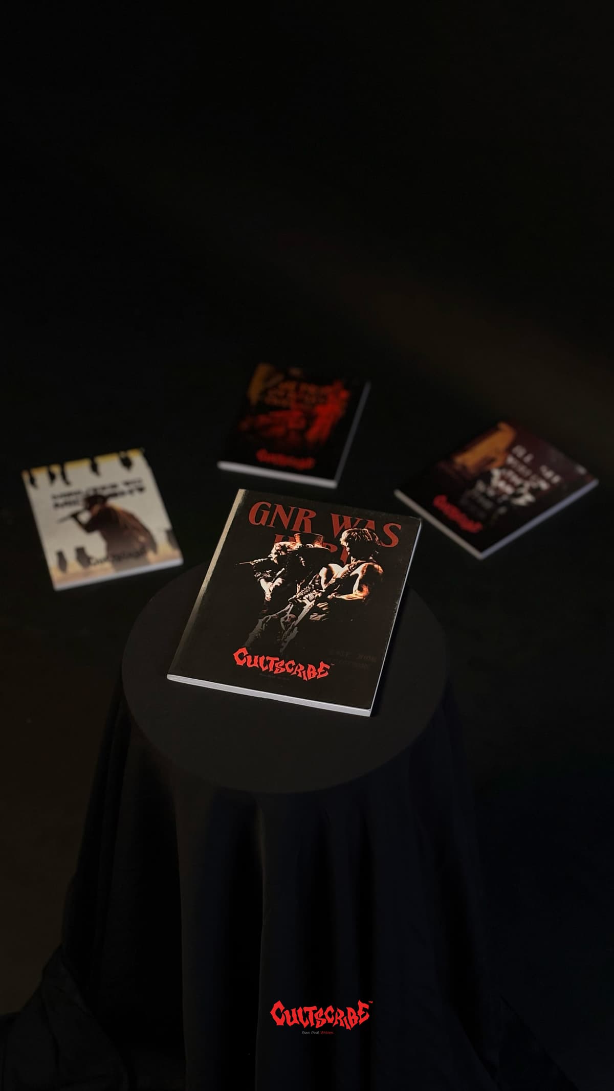 CultScribe product showcase — GNR Was Here notebook on a black pedestal with blurred CultScribe titles behind.